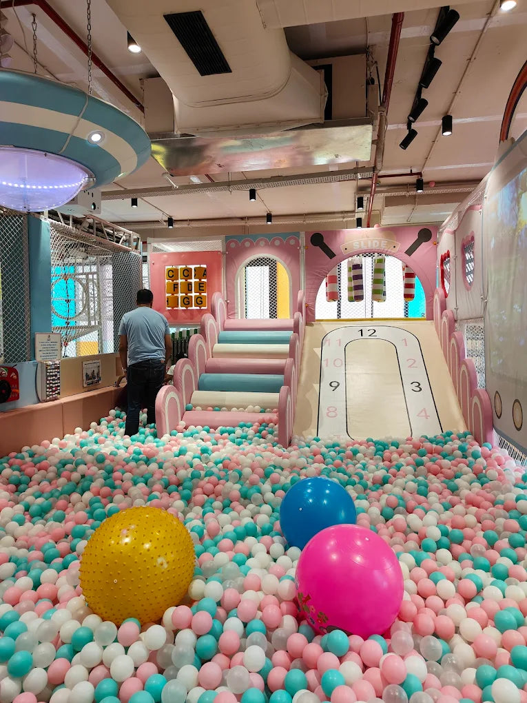 A person stands in a ball pit with a slide and colorful balls.