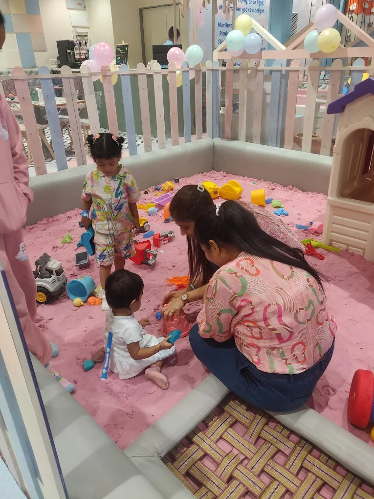 Children and adults play in a pink sandpit with toys.