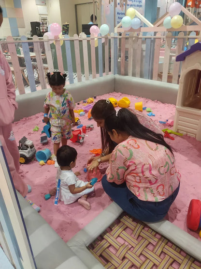 Children and adults play in a pink sandpit with toys.