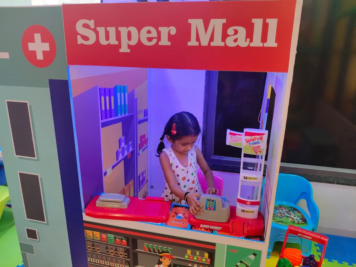 A young girl plays at a toy supermarket inside a "Super Mall" playhouse.