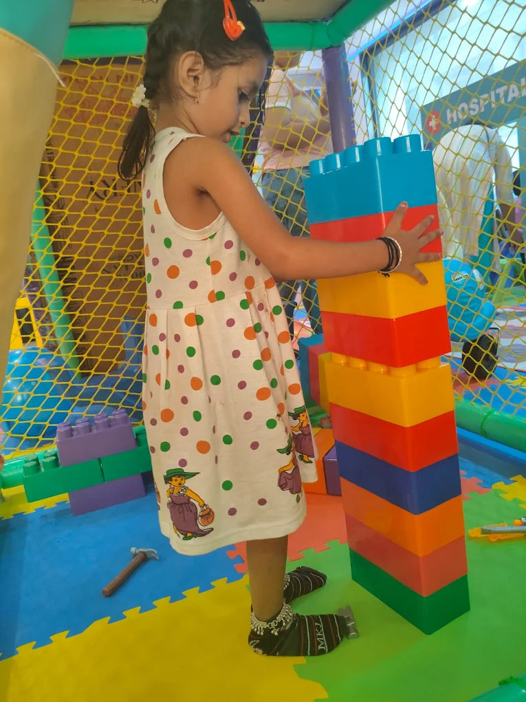 A young girl plays with large building blocks in a colorful indoor play area.