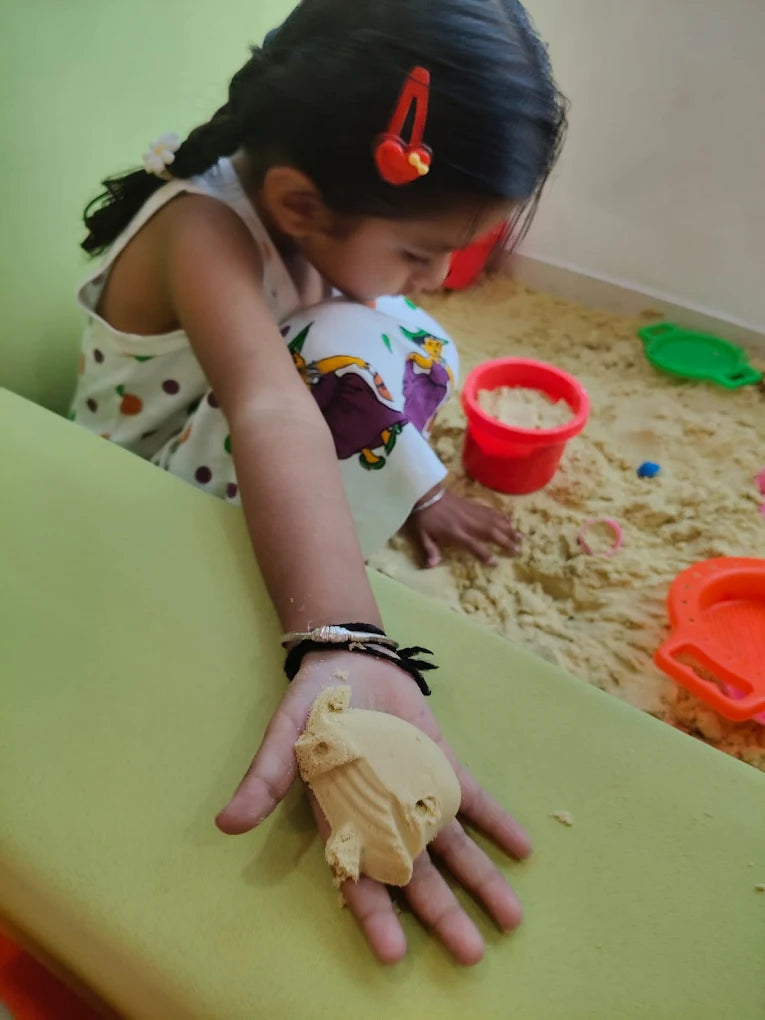 A young child plays with sand, holding a sand mold in their hand.