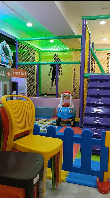 A child plays in a colorful indoor playground with a toy car and climbing structure.