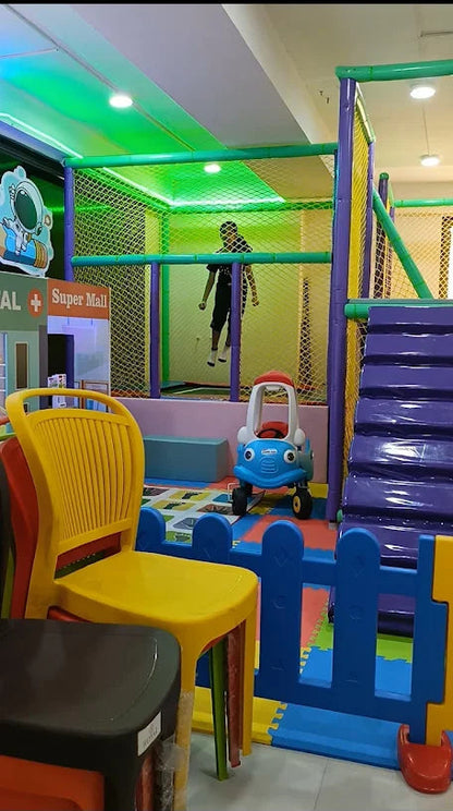 A child plays in a colorful indoor playground with a toy car and climbing structure.