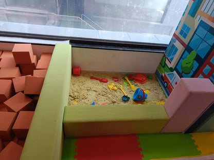 A sandbox with toys for children, surrounded by soft foam blocks and a colorful mural.