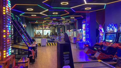 An arcade with colorful neon lights, game machines, and people playing.