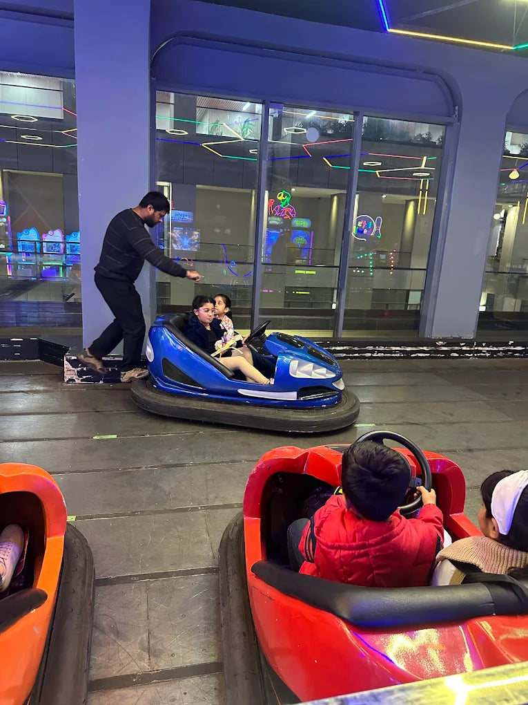 People in bumper cars at an amusement park with a man assisting a child.