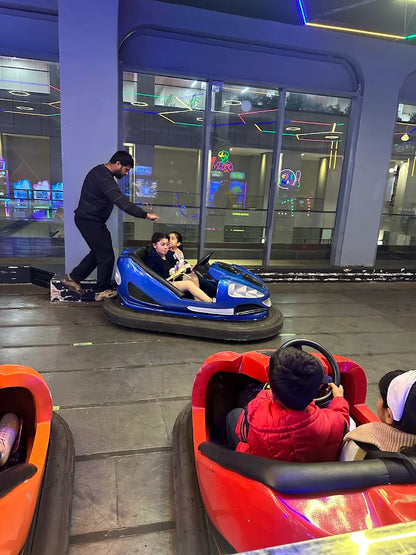 People in bumper cars at an amusement park with a man assisting a child.