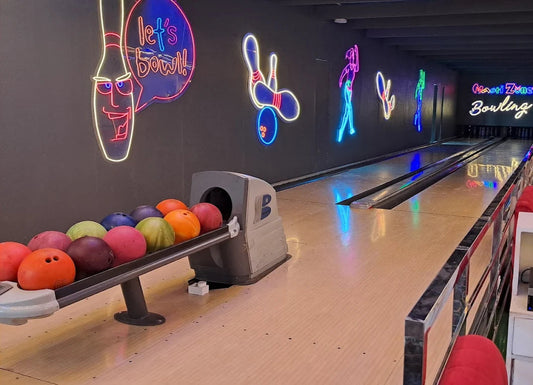 Bowling alley with colorful bowling balls and neon signs on the wall.