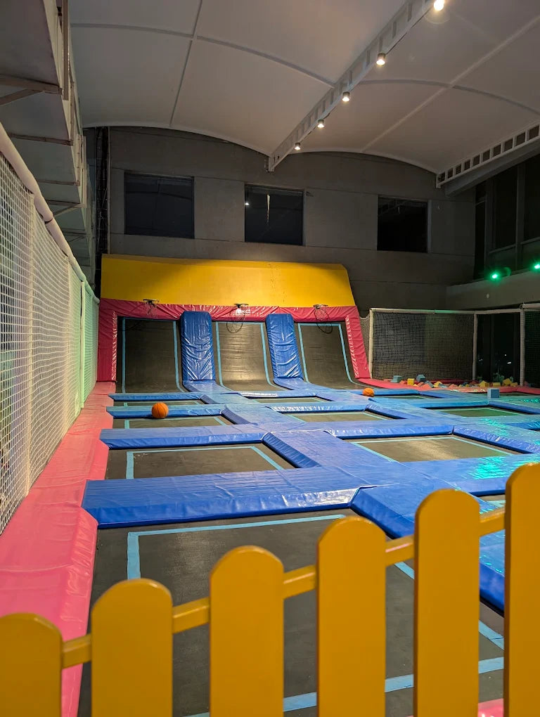 Indoor trampoline park with colorful safety padding and a yellow fence.