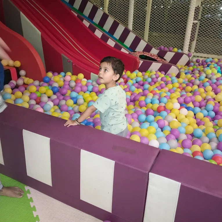 Child playing in a ball pit with a slide in an indoor playground.