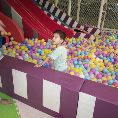 Child playing in a ball pit with a slide in an indoor playground.