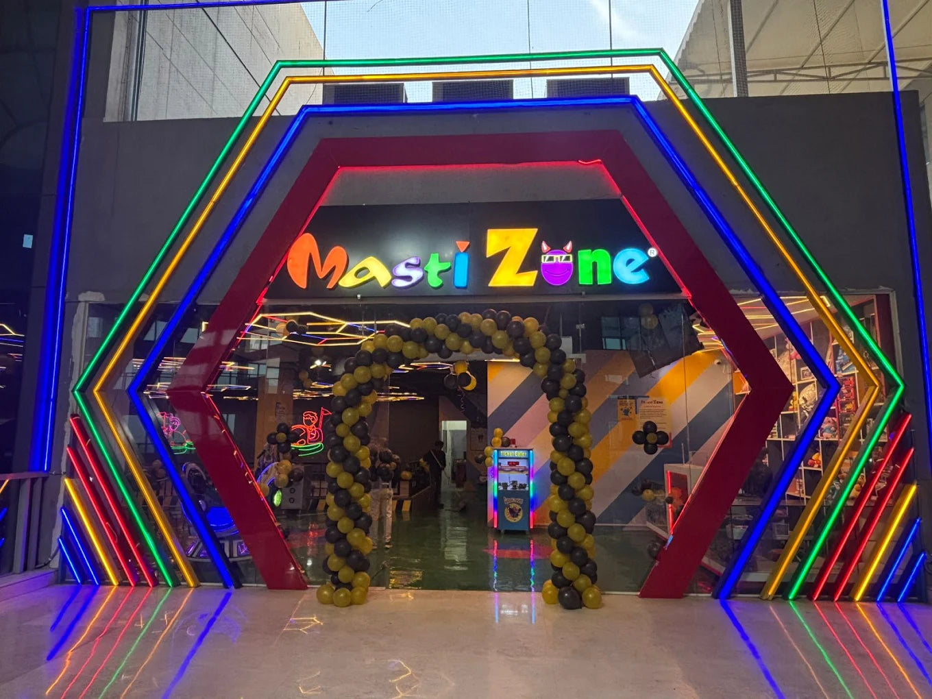 Entrance to Masti Zone, a brightly lit arcade with neon lights and balloon arches, likely for children.