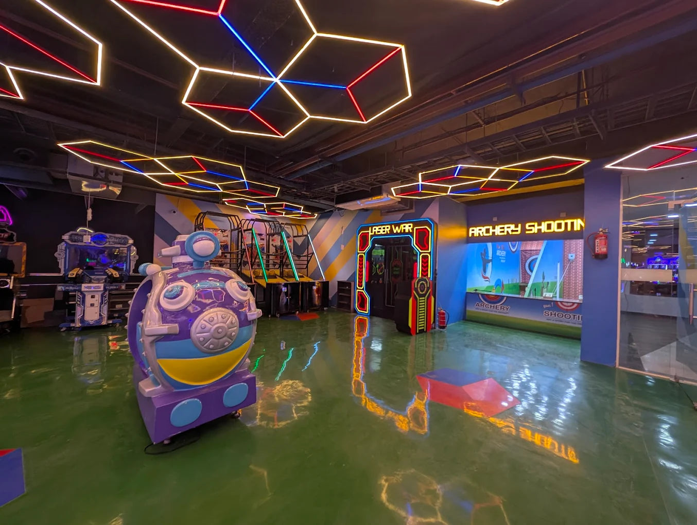 An indoor arcade with neon lights, featuring a laser war game, archery shooting, and a cartoon-themed ride.