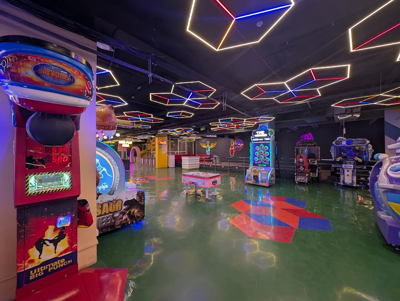An arcade with various games, including a punching machine and racing simulators, illuminated by neon lights.