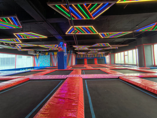 An indoor trampoline park with colorful neon lights and a climbing wall.