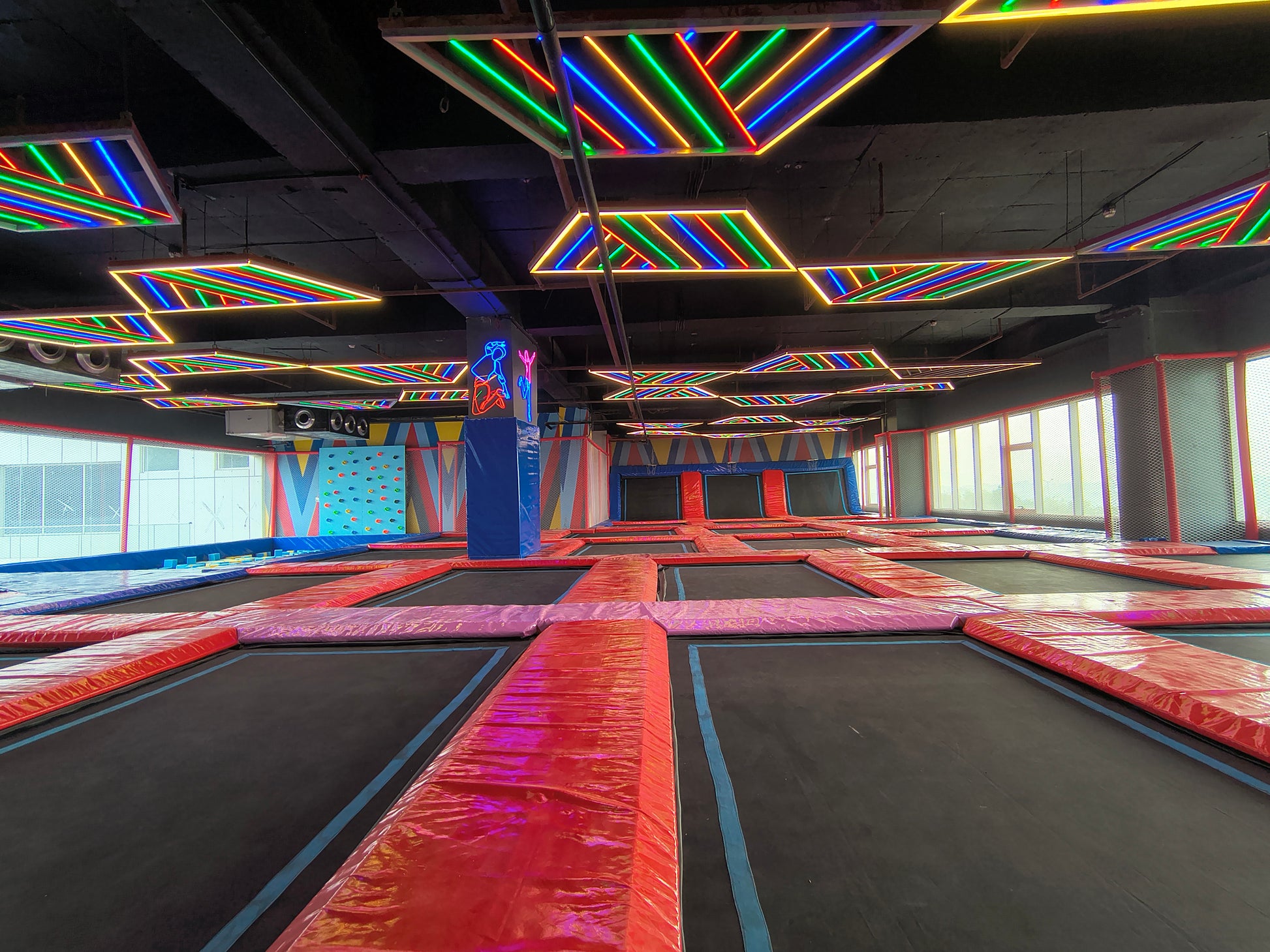 An indoor trampoline park with colorful neon lights and a climbing wall.