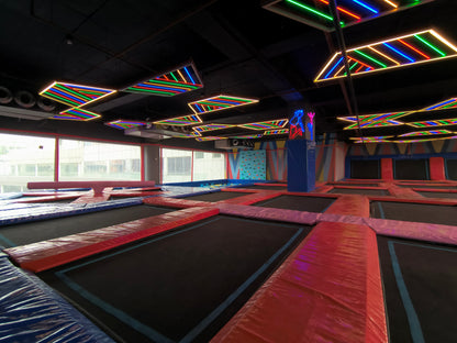 An indoor trampoline park with colorful neon lights and various trampolines.