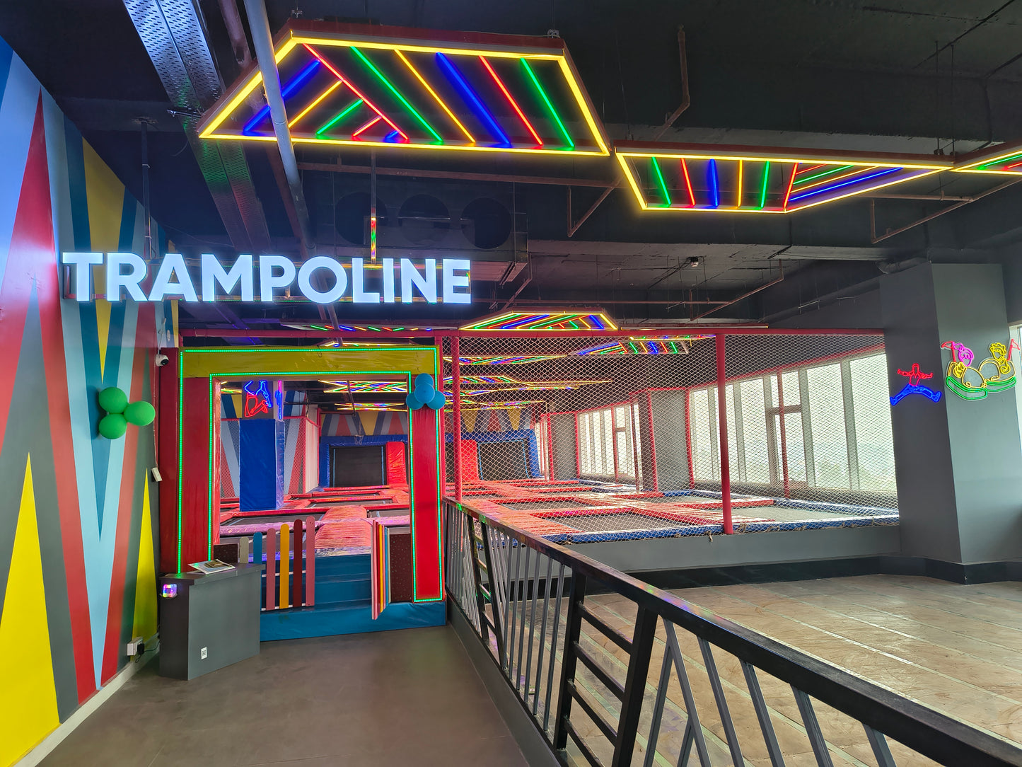 A brightly lit indoor trampoline park with colorful neon lights and multiple trampolines.