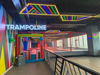 A brightly lit indoor trampoline park with colorful neon lights and multiple trampolines.