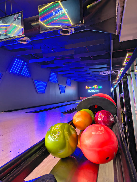 Bowling balls in various colors sit on a rack at a bowling alley with neon lights.