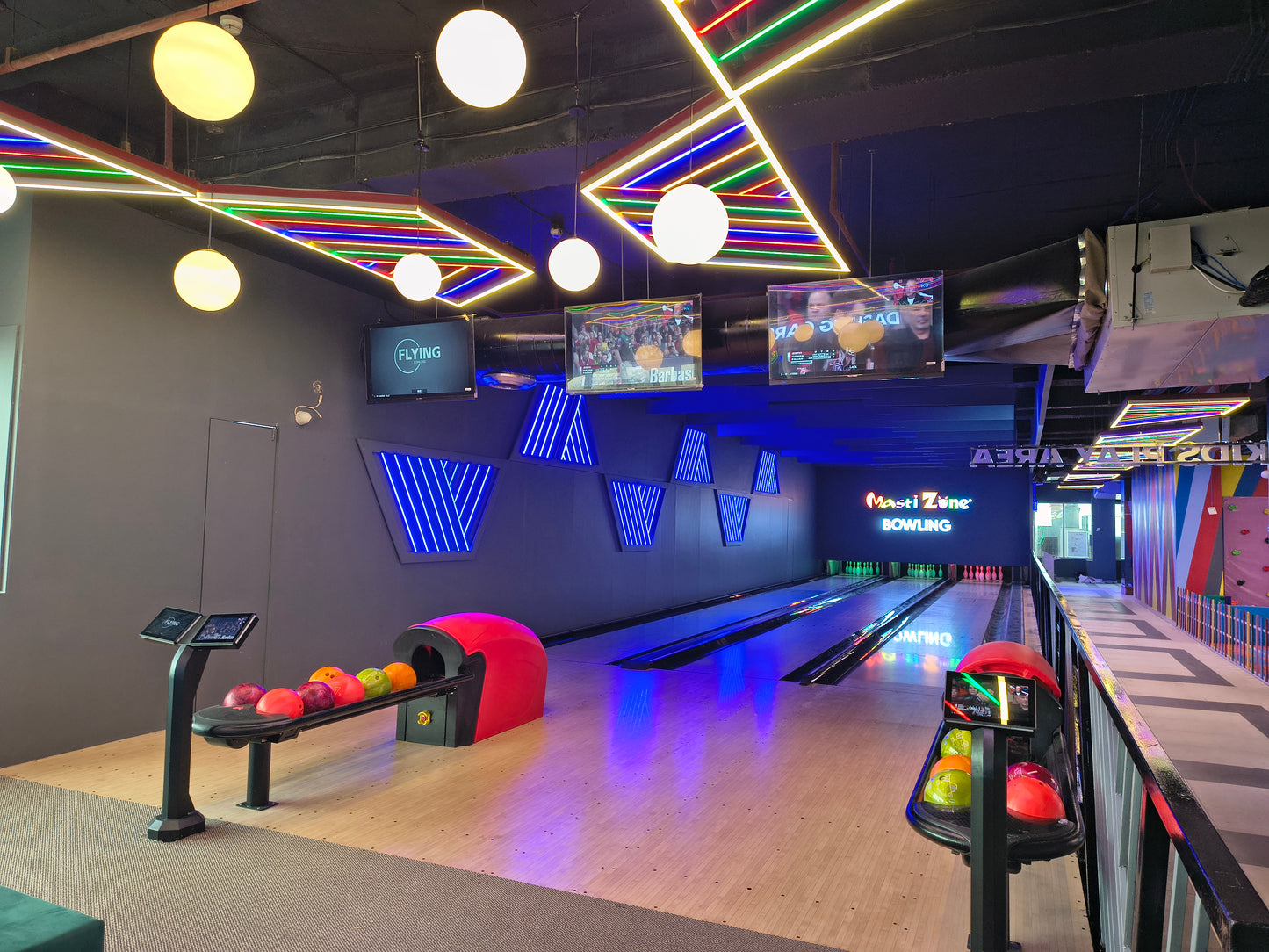 A bowling alley with neon lights and screens showing sports.