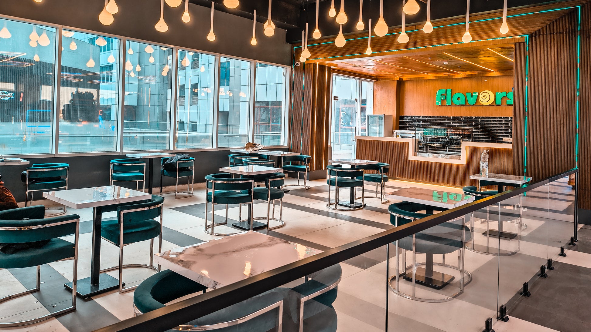 Modern cafe interior with teal velvet chairs and marble tables, illuminated by unique pendant lights.