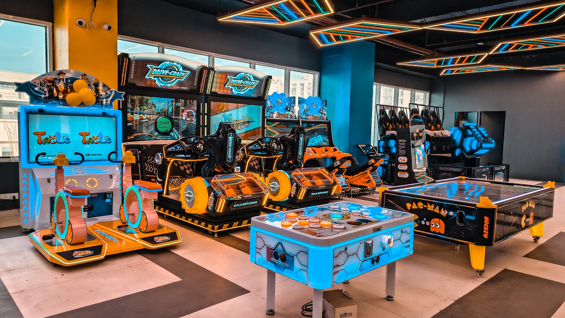 An arcade with various racing and air hockey games, featuring bright neon lights and colorful game cabinets.