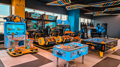 An arcade with various racing and air hockey games, featuring bright neon lights and colorful game cabinets.