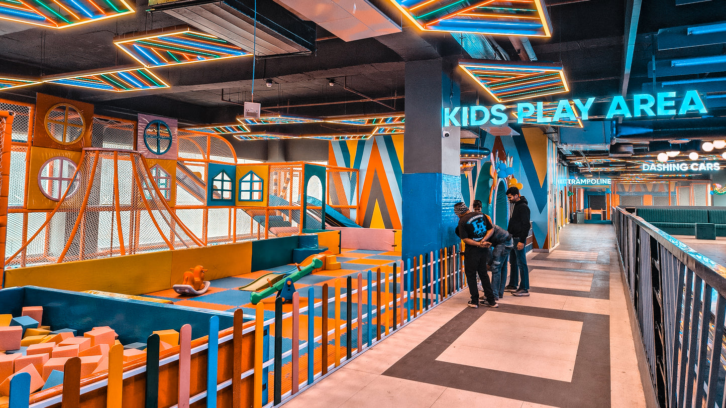 A vibrant indoor play area for kids with colorful structures and neon lights. A few adults stand near the entrance.