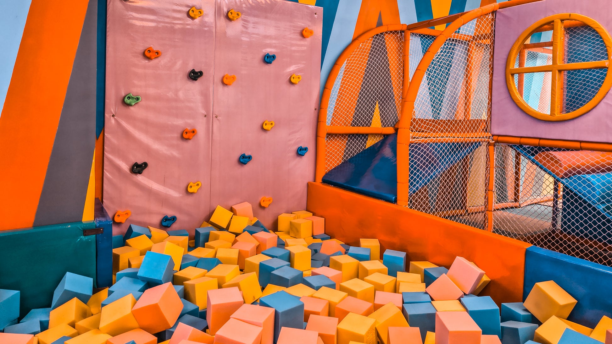Colorful indoor playground with climbing wall, bouncy castle, and foam pit.