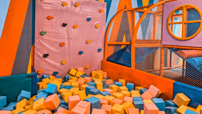 Colorful indoor playground with climbing wall, bouncy castle, and foam pit.