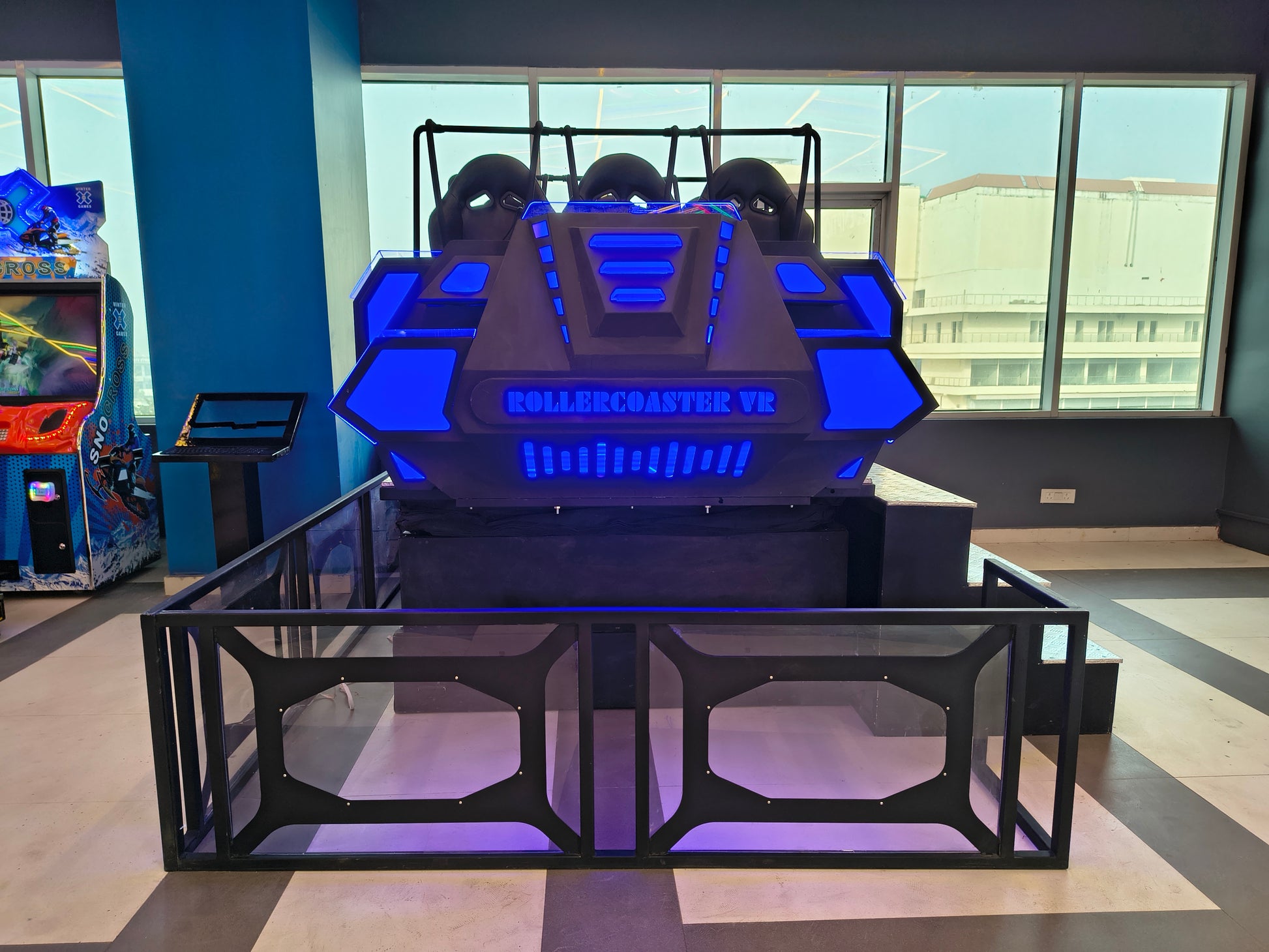 A virtual reality rollercoaster ride with blue lights and seats, in an arcade.