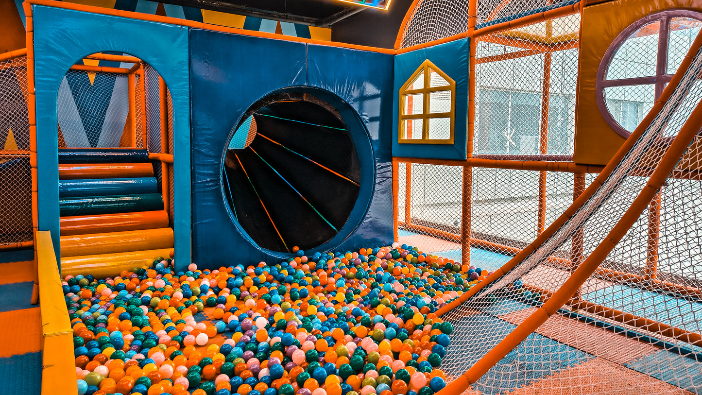 A colorful ball pit in a children's indoor playground with a tunnel and slide.