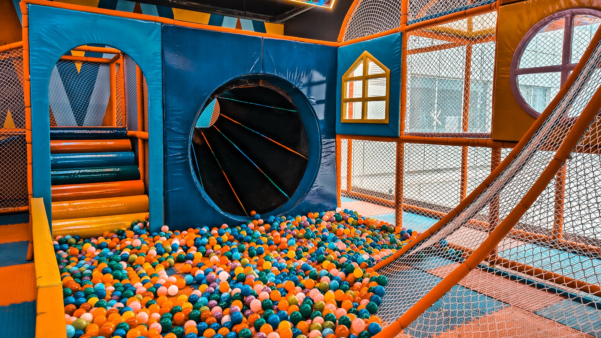 A colorful ball pit in a children's indoor playground with a tunnel and slide.