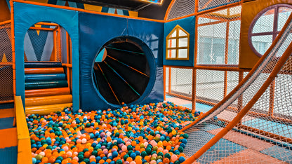 A colorful ball pit in a children's indoor playground with a tunnel and slide.