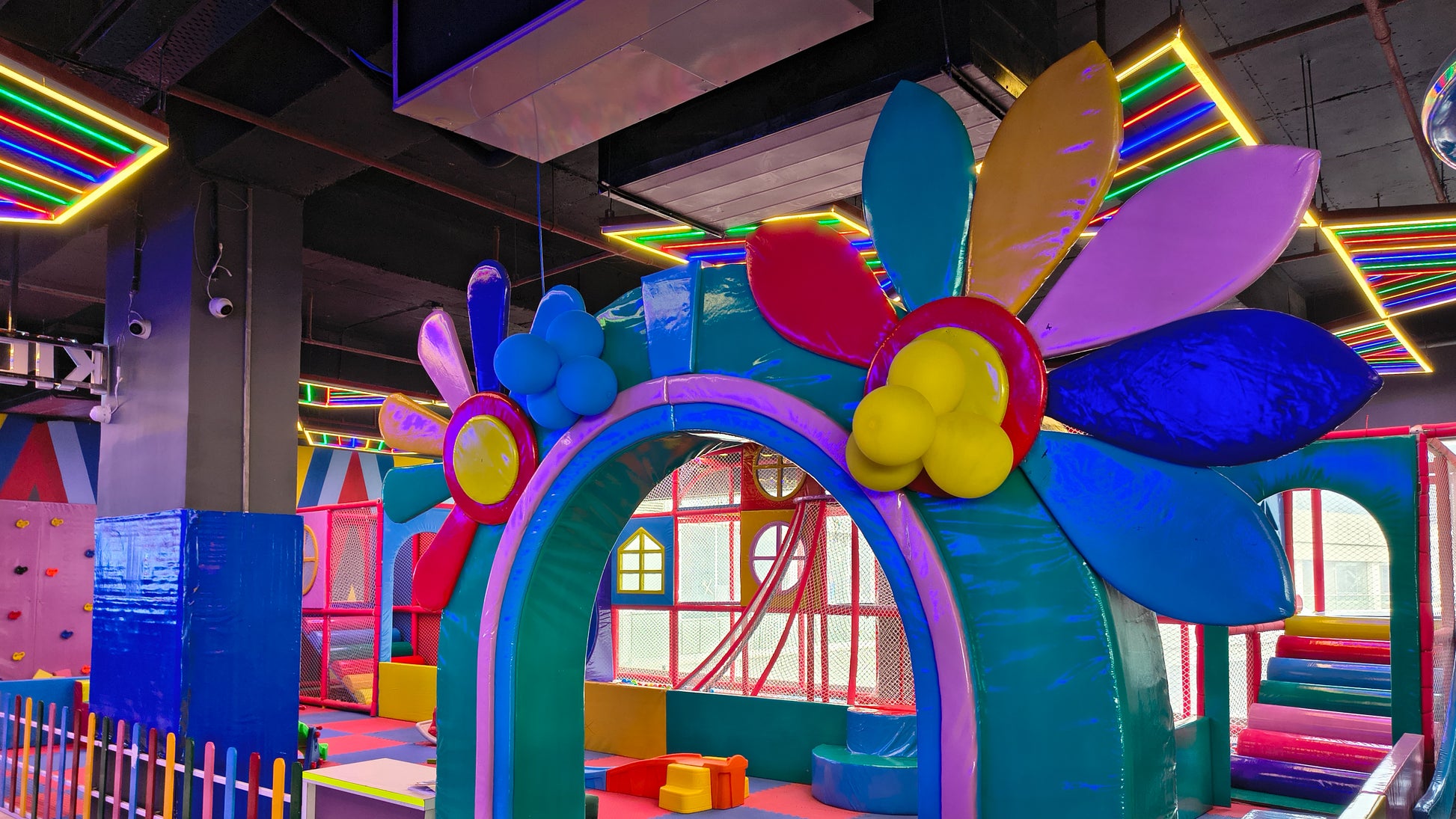 A colorful indoor playground with soft play structures and neon lights.