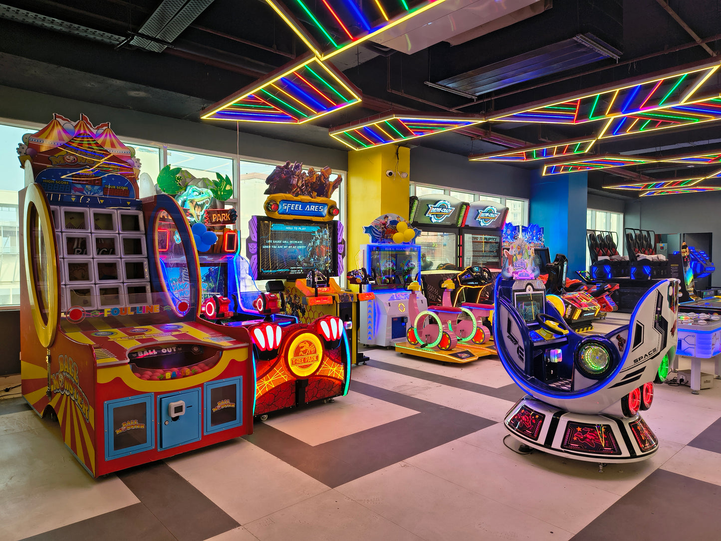 Colorful arcade machines in an indoor gaming area with a checkered ceiling.