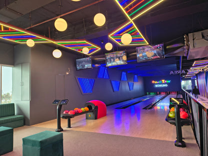 A modern bowling alley with neon lights and screens, featuring bowling balls on a rack.