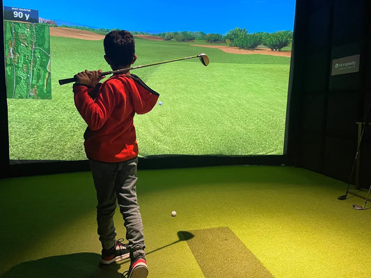 Teenage child playing golf simulator indoors with a screen displaying a golf course.