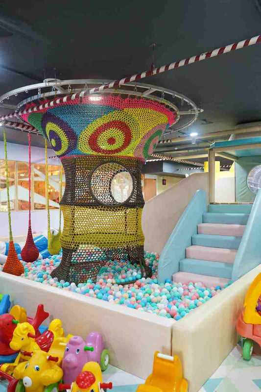 A colorful indoor playground with a ball pit, slide, and climbing net for children.