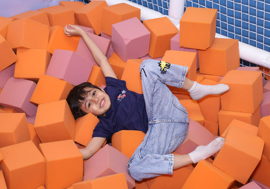 A young boy smiles while playing in a ball pit filled with orange and pink foam cubes.