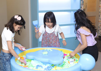 Three young girls play with kinetic sand at a blue play table.