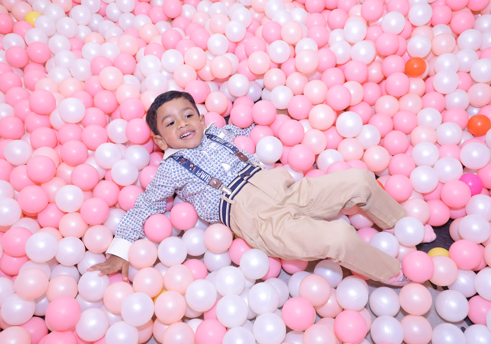 A young boy lies in a ball pit filled with pink and white balls.