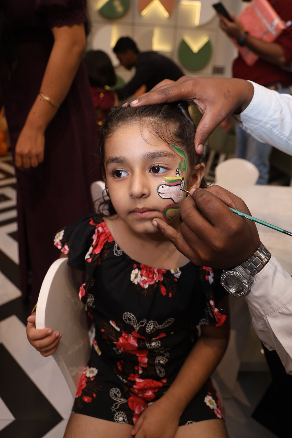 A child gets their face painted with a unicorn design at a party.