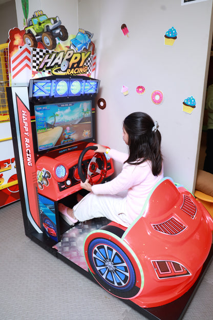 A young girl plays a racing arcade game in a bright red car-shaped seat.