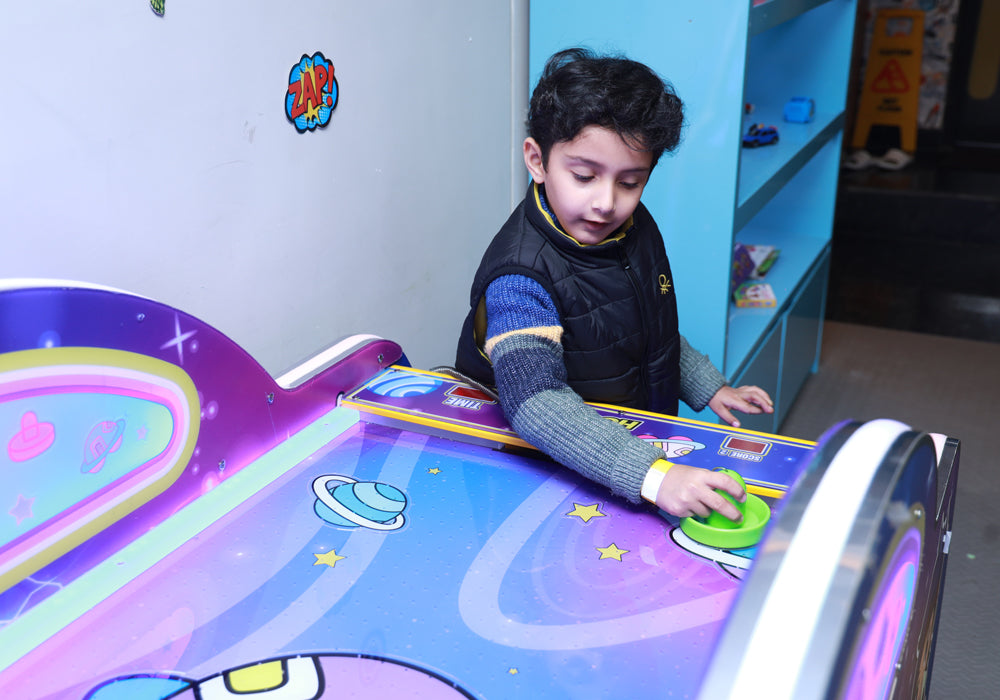 A young boy plays an air hockey game with a colorful, space-themed table.