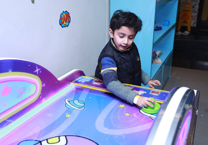A young boy plays an air hockey game with a colorful, space-themed table.