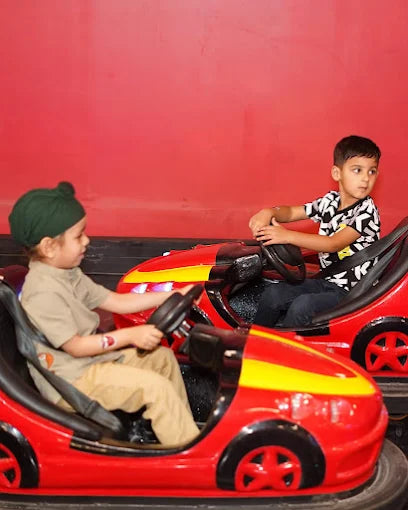 Two young children in bumper cars on a red background.