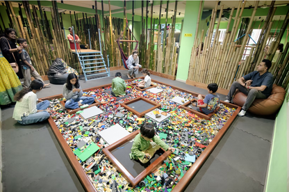 Children play with a large pile of LEGOs in a room decorated with bamboo. Adults watch or relax nearby.